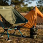 Lightweight camping chair set up outdoors near tent with compact folded size shown beside it