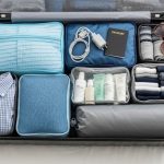 A neatly organized open suitcase with clothing, toiletries, and travel accessories arranged in packing cubes on a white bed