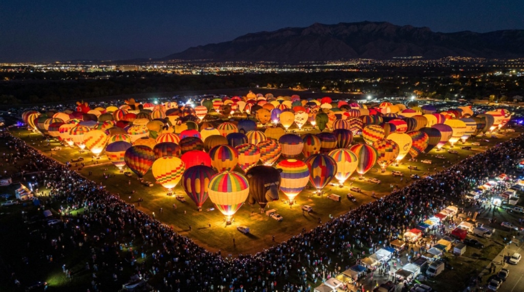 Aerial view of glowing hot air balloons tethered to the ground at night during the Albuquerque Balloon Fiesta Balloon Glow event